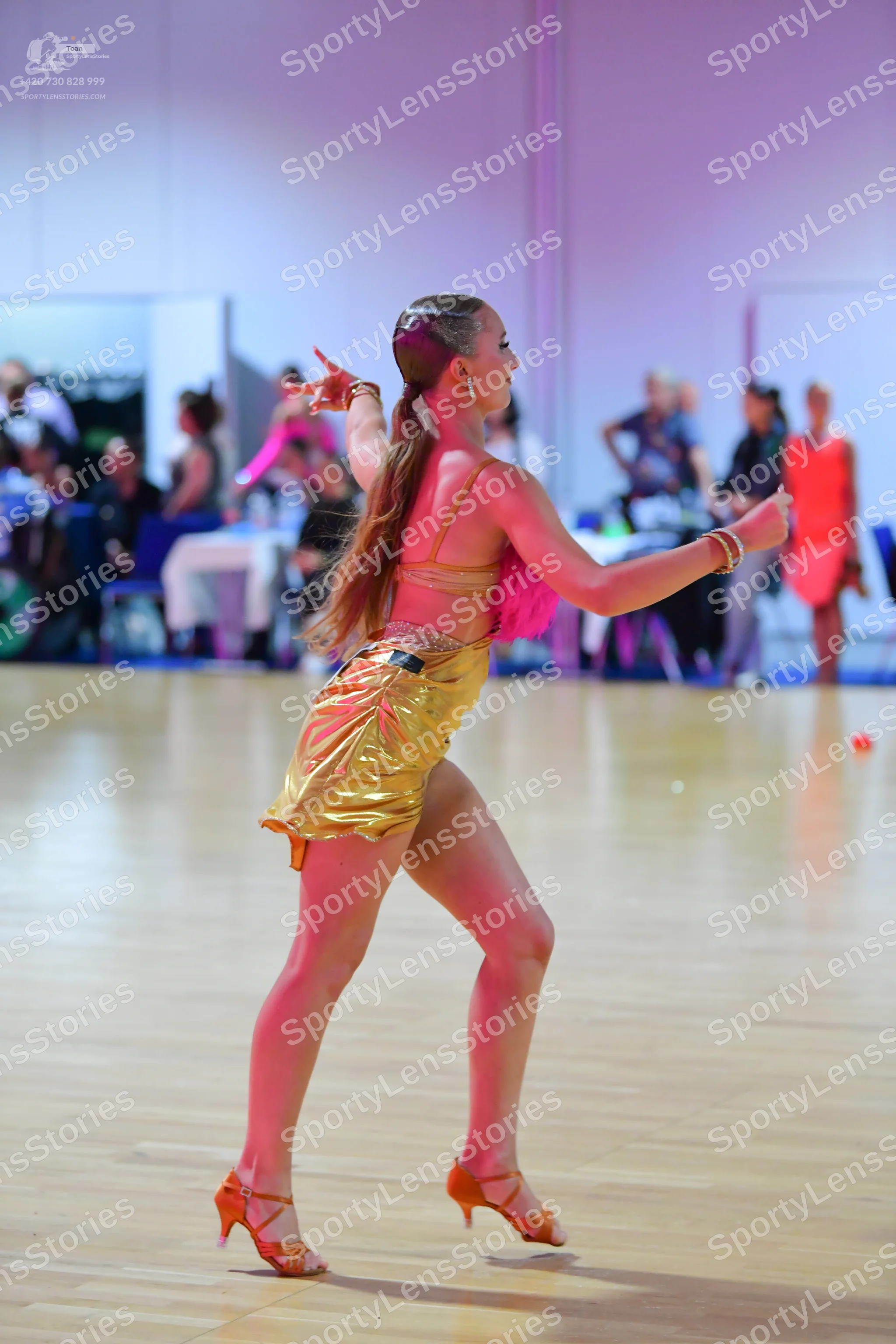 Dancesport competitor: Female dancer in foreground: gold metallic two-piece Latin dance outfit consisti