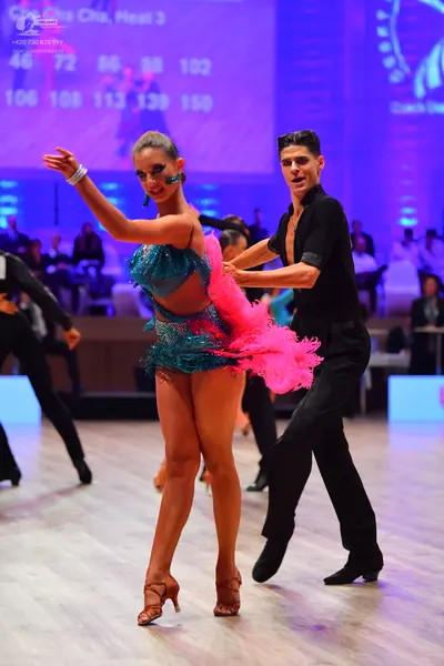 Dancesport competitor: Female dancer: teal sequined Latin dress with voluminous bright pink feathers on
