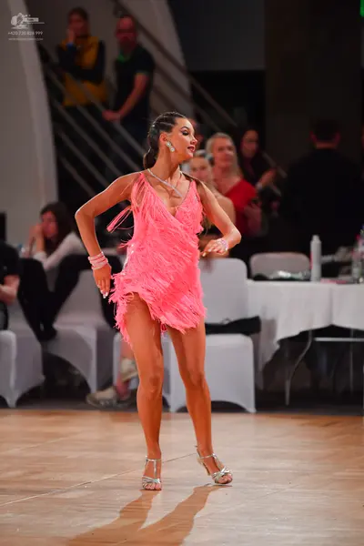 Dancesport competitor: Female dancer: pink latin dress with fringe, pink wristband, and silver strappy 