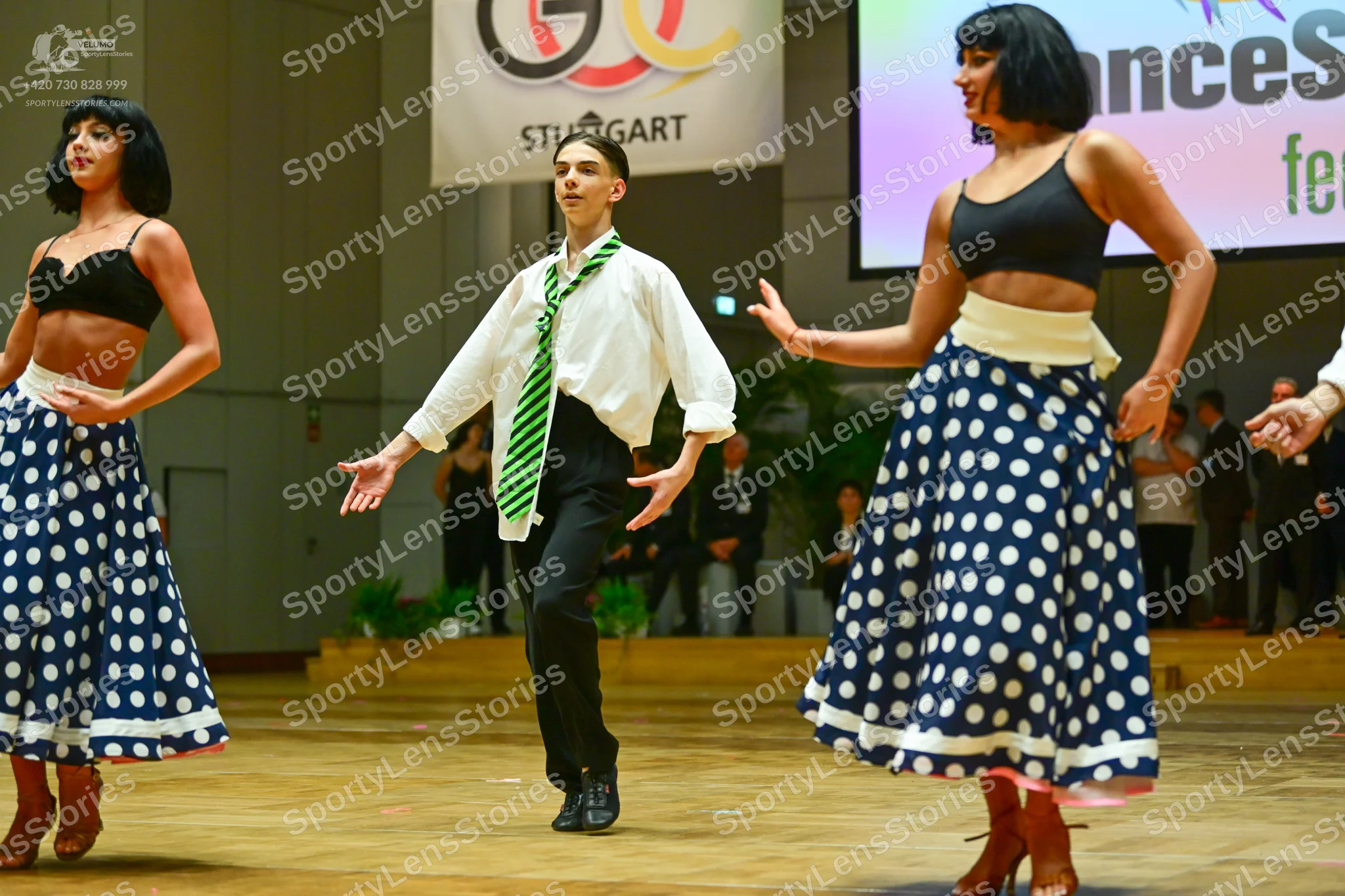 Dancesport competitor: Female dancers: black bra-style crop tops and long, navy blue skirts with large 