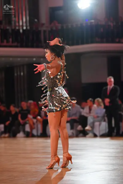Dancesport competitor: Female dancer: black latin dress covered in large silver paillettes and wearing 
