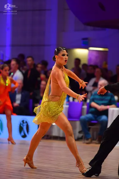 Dancesport competitor: Female dancer in center: gold sequined Latin dress with a halter neck, gold brac