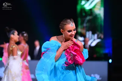 Dancesport competitor: Female dancer in foreground: light blue dress with large, sheer, flowing sleeves