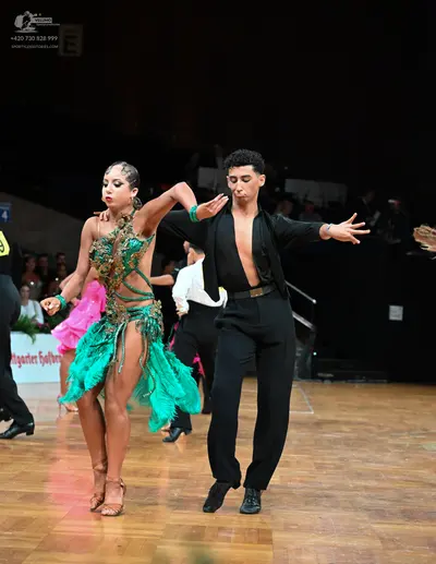Dancesport competitor: Female dancer: green Latin dance dress with a gold sequined bodice and long gree