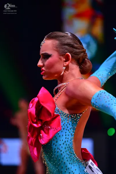 Dancesport competitor: Female dancer: light blue sequined latin dress with a large magenta satin bow on