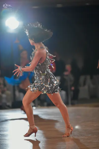 Dancesport competitor: Female dancer in foreground: silver Latin dance dress heavily embellished with l