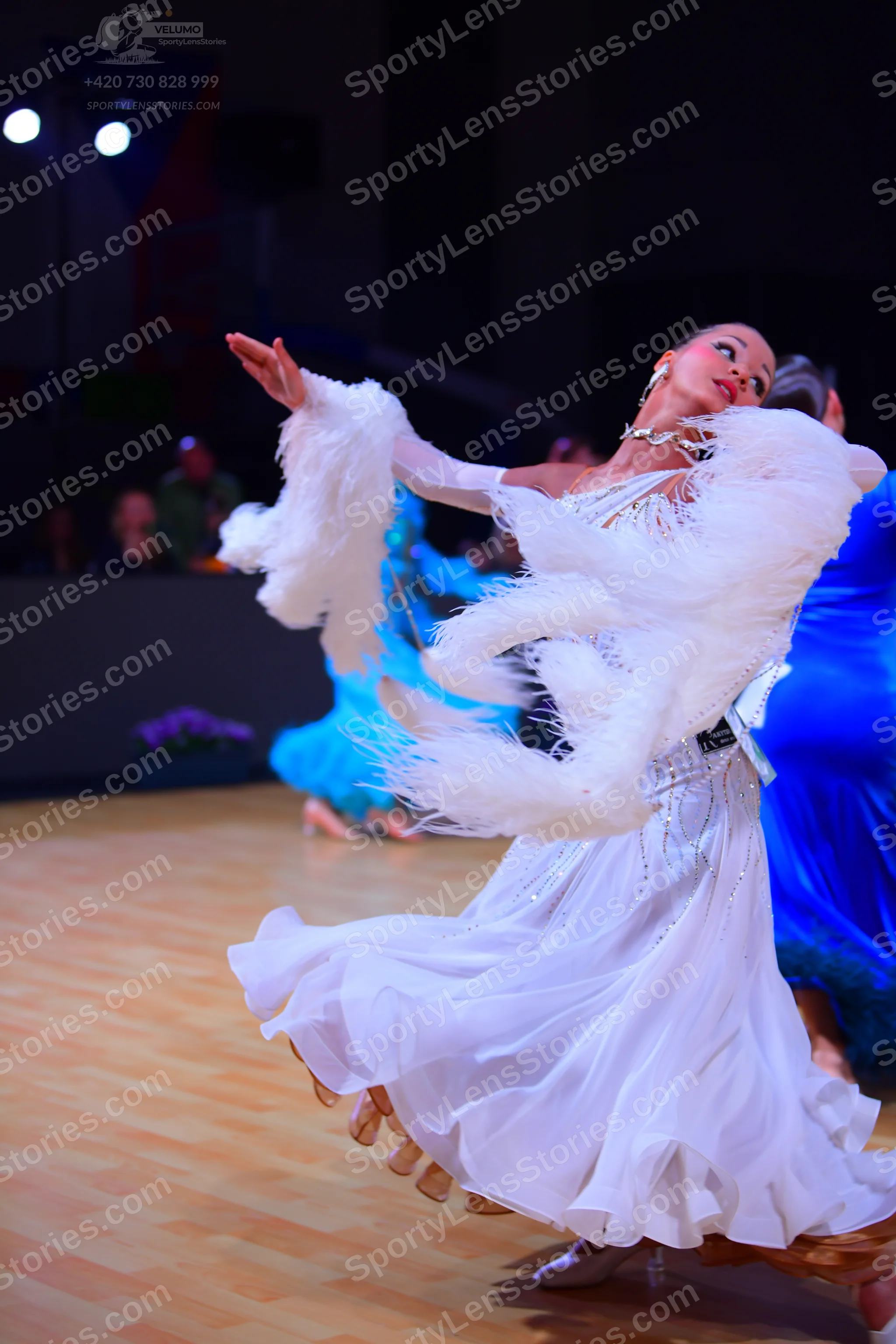 Dancesport competitor: Female dancer in foreground: white ballgown with voluminous white feather-like f