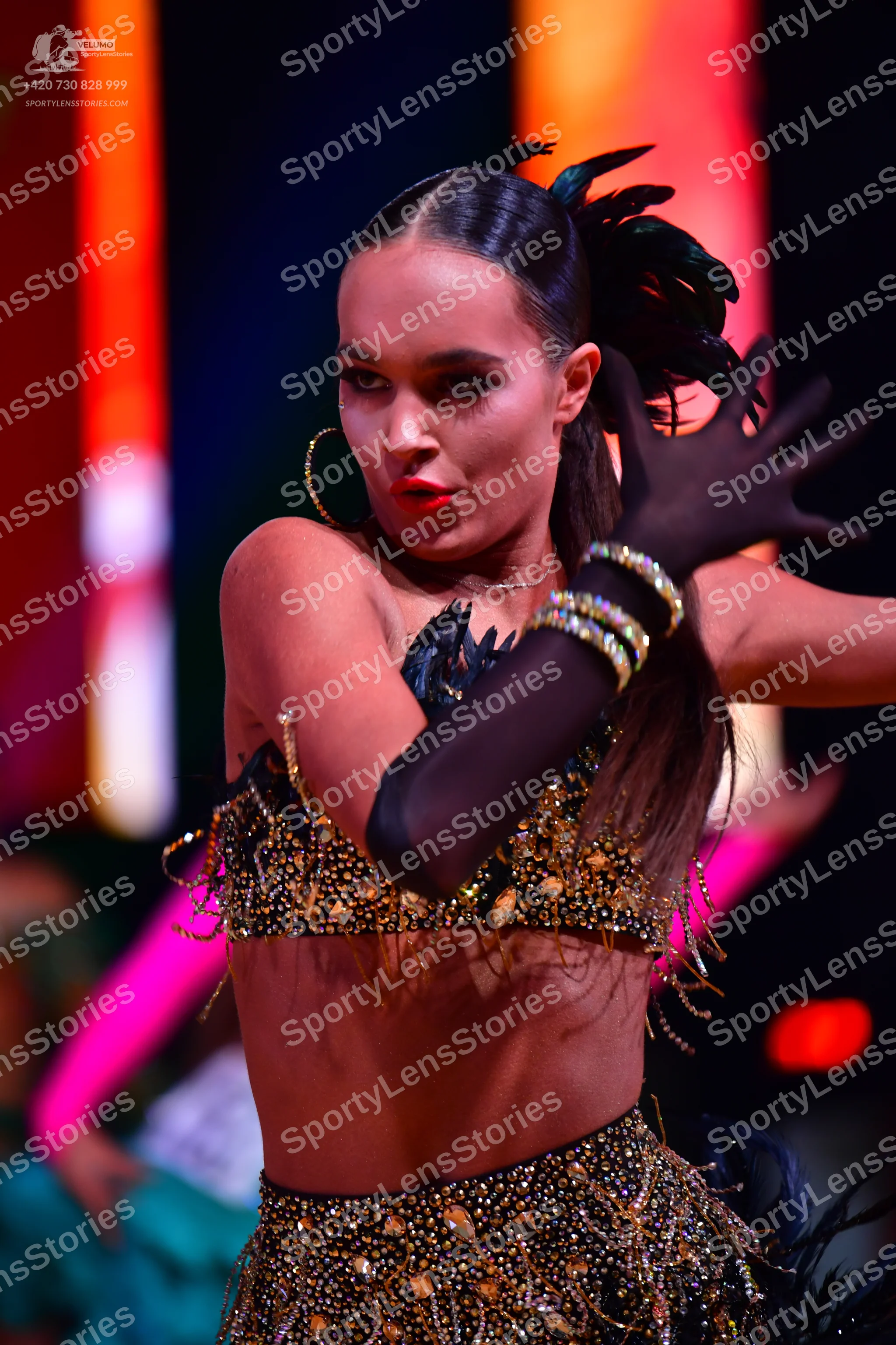 Dancesport competitor: Female dancer: black two-piece Latin costume heavily adorned with gold sequins a