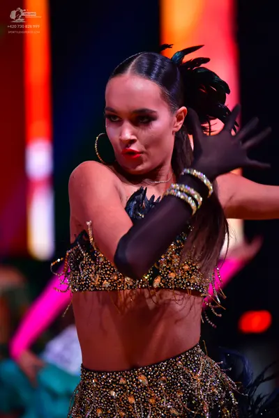 Dancesport competitor: Female dancer: black two-piece Latin costume heavily adorned with gold sequins a