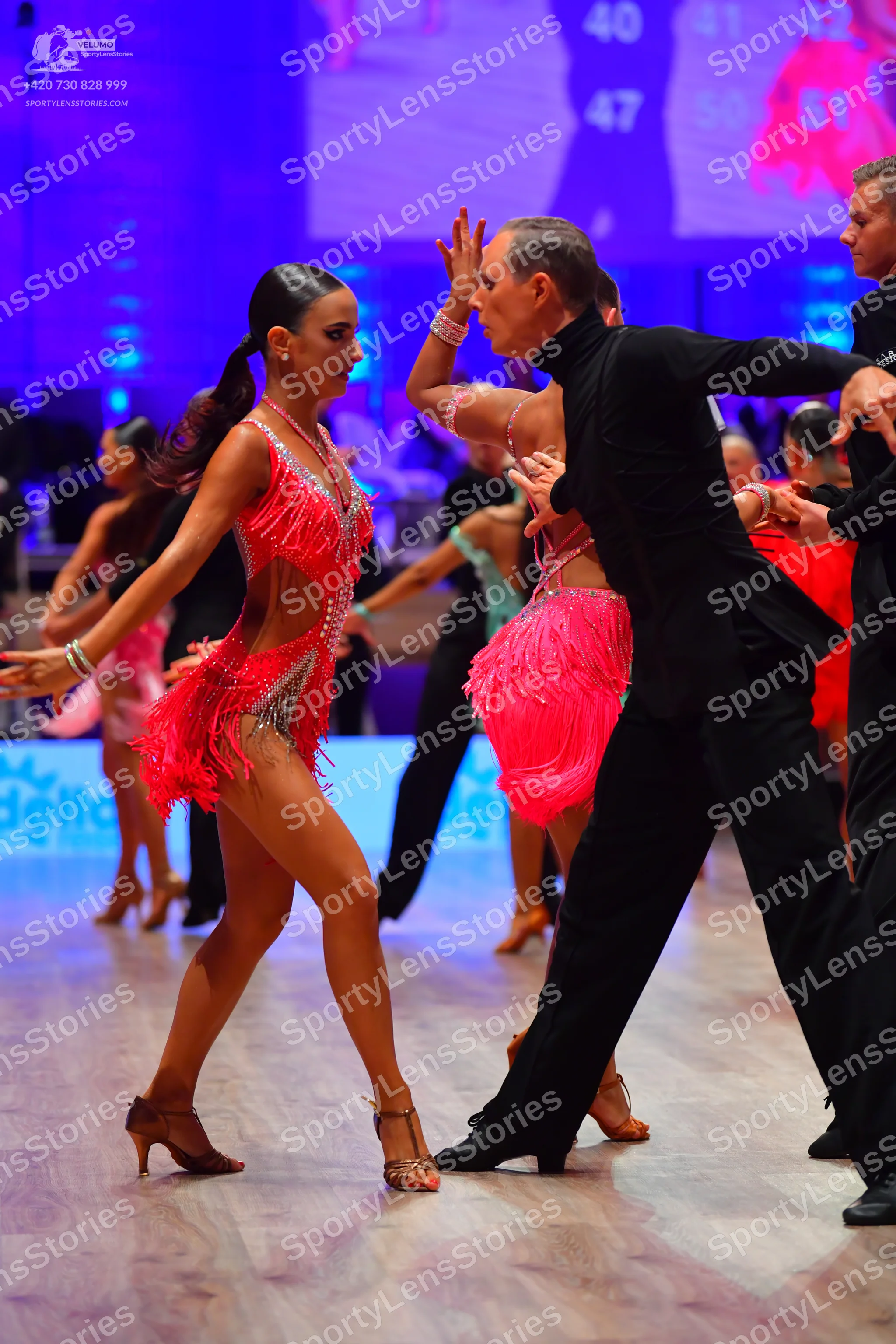Dancesport competitor: Female dancer in foreground: hot pink Latin dance dress with fringe, sequins, an