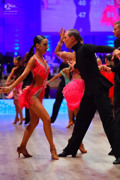 Dancesport competitor: Female dancer in foreground: hot pink Latin dance dress with fringe, sequins, an