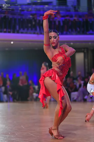 Dancesport competitor: Female dancer: red Latin dress with lace and sequins, a ruffled skirt, and red b
