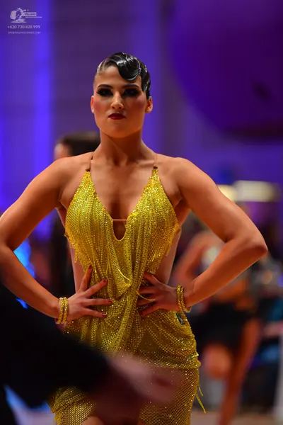 Dancesport competitor: Female dancer: gold sequined Latin dress with thin straps and a deep V-neckline,
