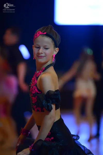 Dancesport competitor: Female dancer in foreground: black Latin dance costume with bright pink sequin p