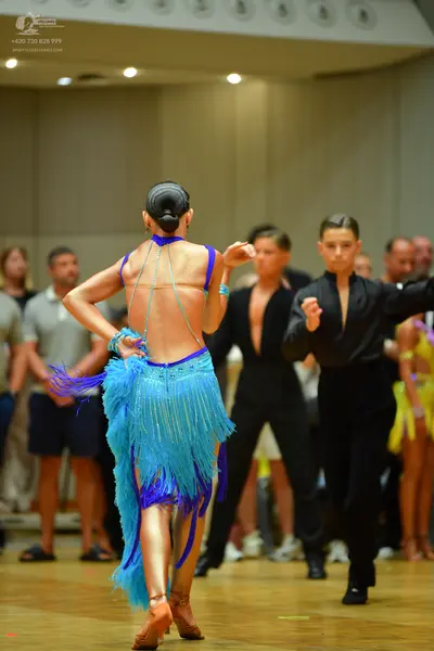 Dancesport competitor: Female dancer in foreground: light blue latin dress with long fringe and halter 
