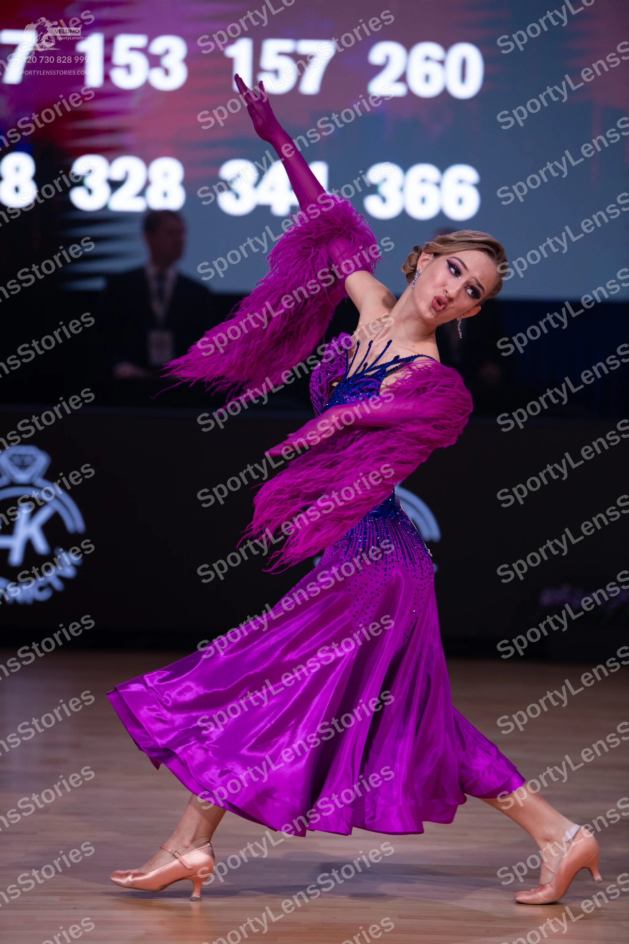 Dancesport competitor: Female dancer: purple/magenta ballroom dress with a shiny skirt and large feathe