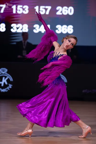 Dancesport competitor: Female dancer: purple/magenta ballroom dress with a shiny skirt and large feathe