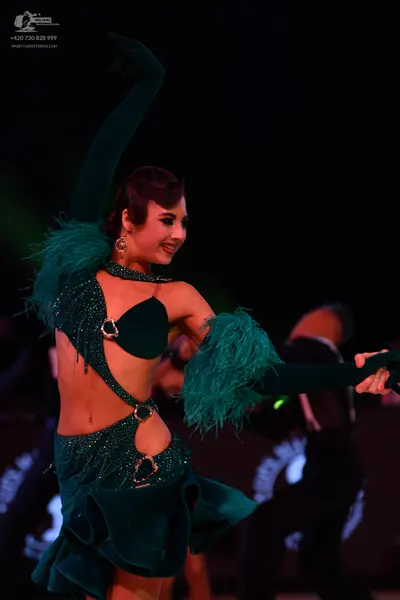 Dancesport competitor: Female dancer: dark green latin dance dress with sequins, feathers on the sleeve