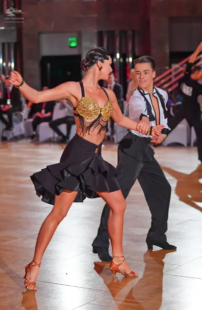 Dancesport competitor: Female dancer: gold sequined bra-style top with black fringe, black flared Latin