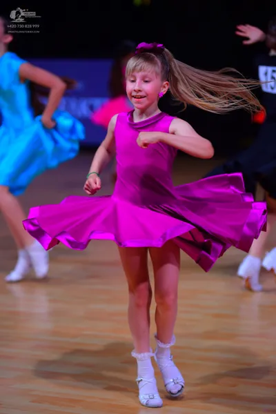 Dancesport competitor: Female dancer in center: bright magenta sleeveless dress with a large, flared sk