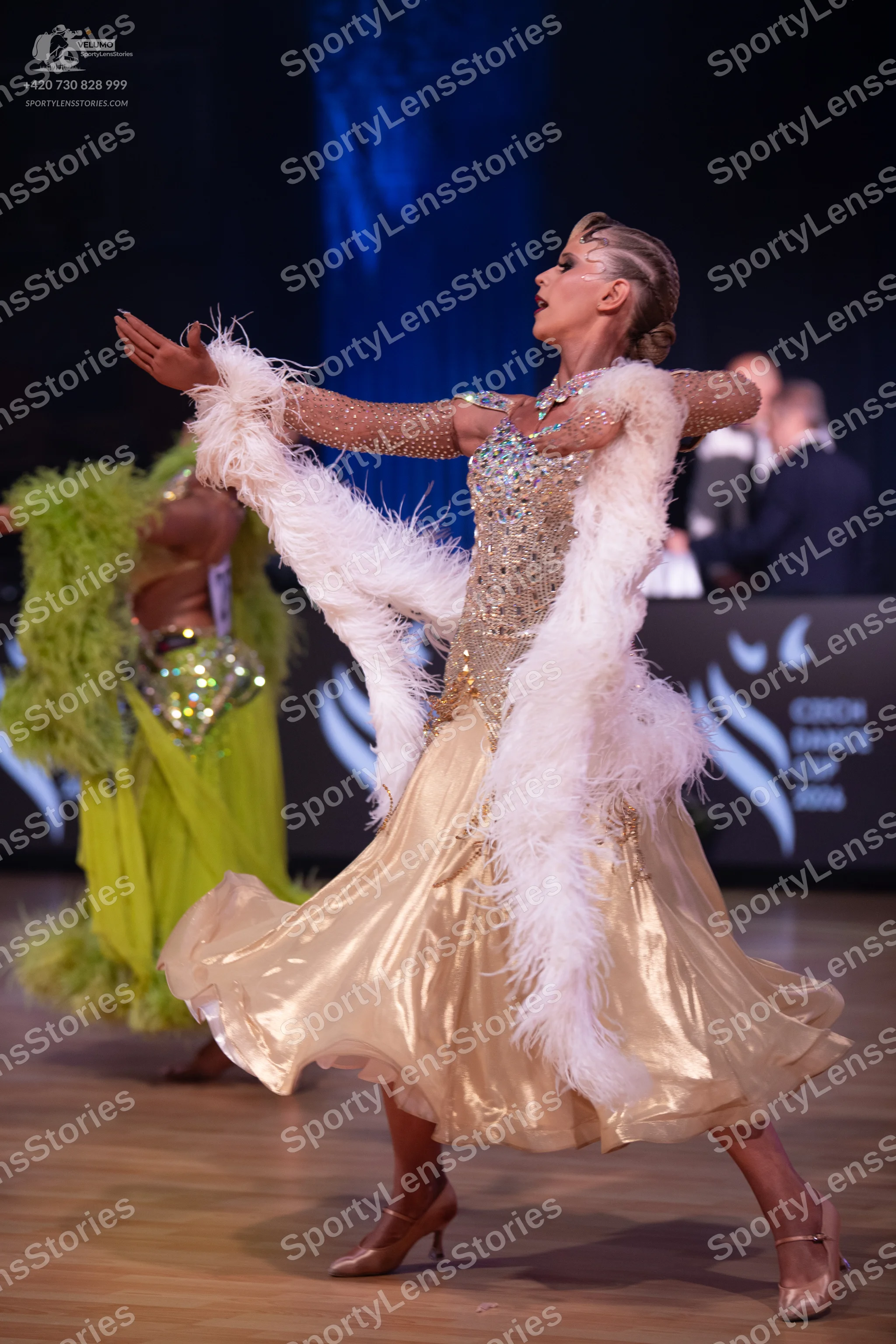 Dancesport competitor: Female dancer in foreground: gold ballgown with a sequin and crystal-encrusted b