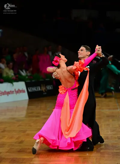 Dancesport competitor: Female dancer: bright pink latin dance dress with orange fabric drapes and ruffl