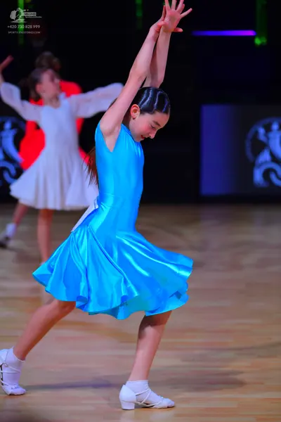Dancesport competitor: Female dancer 1: blue satin sleeveless Latin dress with a flared skirt and white