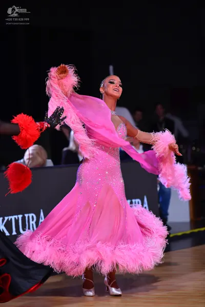Dancesport competitor: Female dancer: pink ballroom dress with sheer, flowing sleeves and a voluminous 