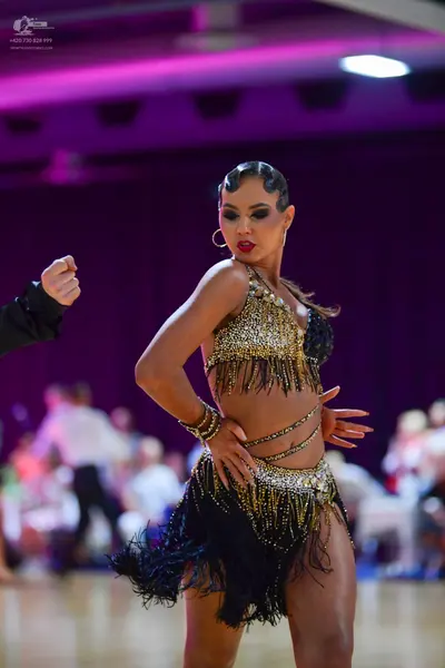 Dancesport competitor: Female dancer: gold and black Latin dance costume featuring a heavily sequined g