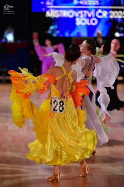 Dancesport competitor #128: Female dancer in foreground: yellow satin-like dress with large, vibrant orange 