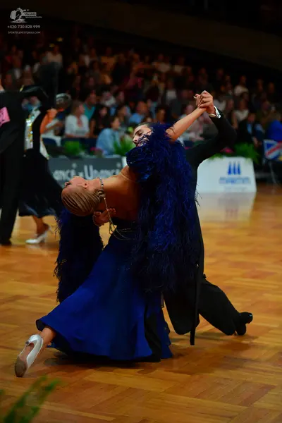 Dancesport competitor: Female dancer: dark blue ballgown with large blue feathers on the back and skirt
