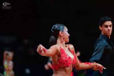 Dancesport competitor: Female dancer: red Latin costume with intricate red lace floral appliqué on a nu