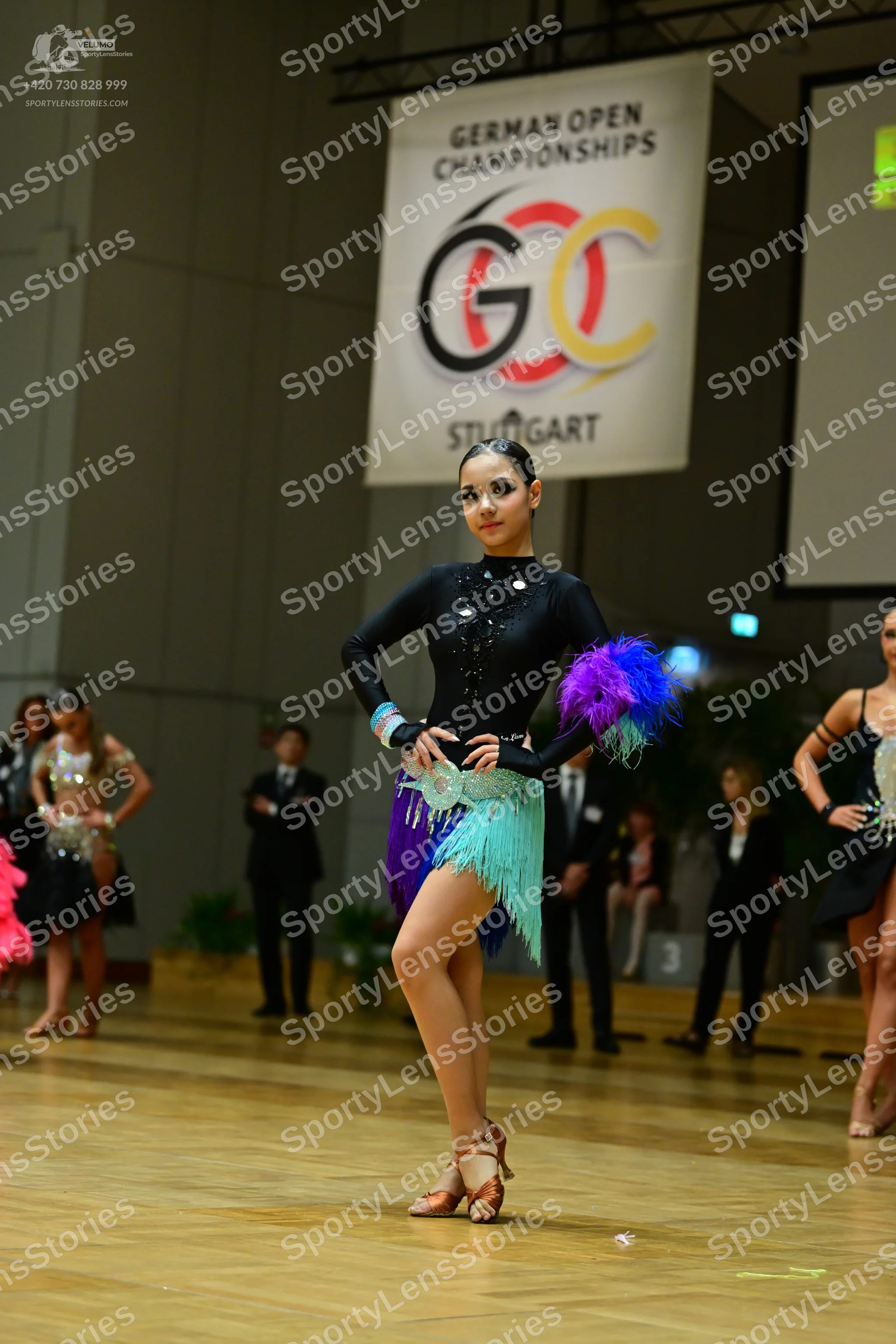 Dancesport competitor: Foreground female dancer: black long-sleeved Latin dress with silver/sequin wais