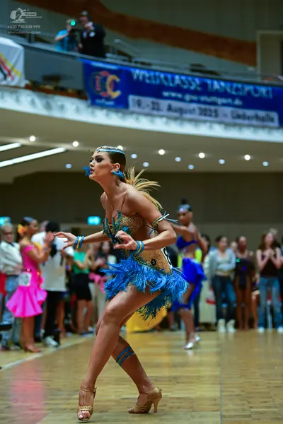 Dancesport competitor: Foreground dancer: gold and blue Latin dress with sequins, blue fringe, and matc