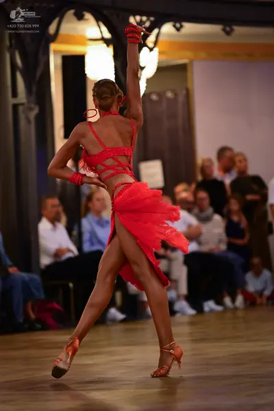 Dancesport competitor: Female dancer: red latin dress with straps and a short, layered skirt, and match