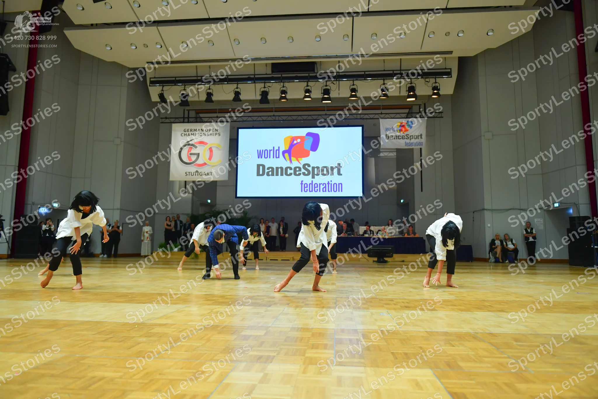 Dancesport competitor: Five dancers are visible in the foreground performing a choreography