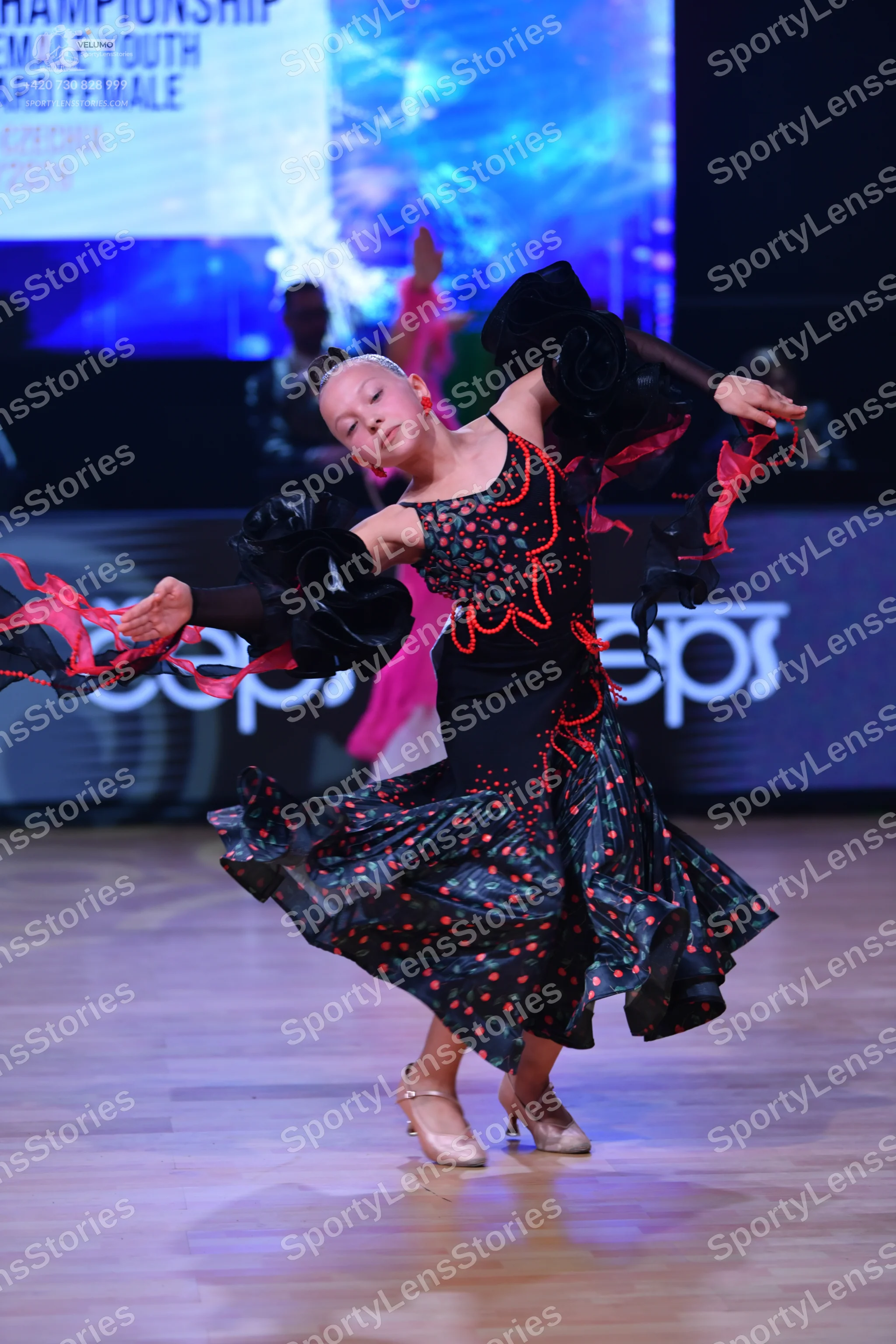 Dancesport competitor: Female dancer: black Latin dance dress with red and pink patterns, featuring lar