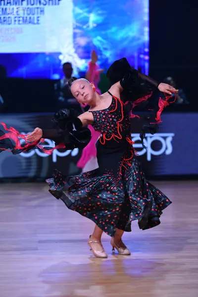 Dancesport competitor: Female dancer: black Latin dance dress with red and pink patterns, featuring lar