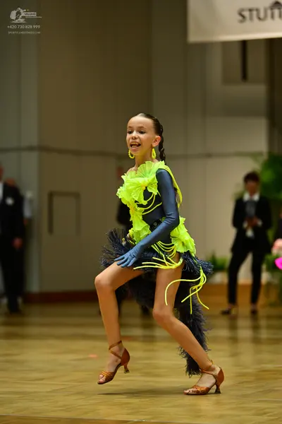 Dancesport competitor: Female dancer: lime green ruffled top, metallic blue long sleeves, dark navy/bla