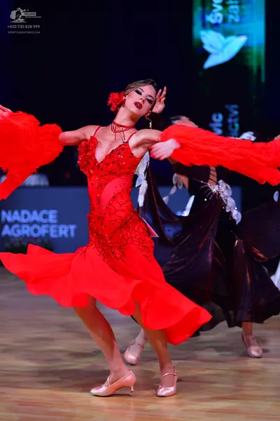 Dancesport competitor: Female dancer in foreground: red latin dress with red sequin embellishments, nud