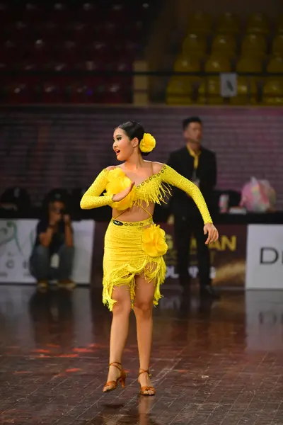 Dancesport competitor: Female dancer: bright yellow latin dress with long sleeves, fringe details, and 