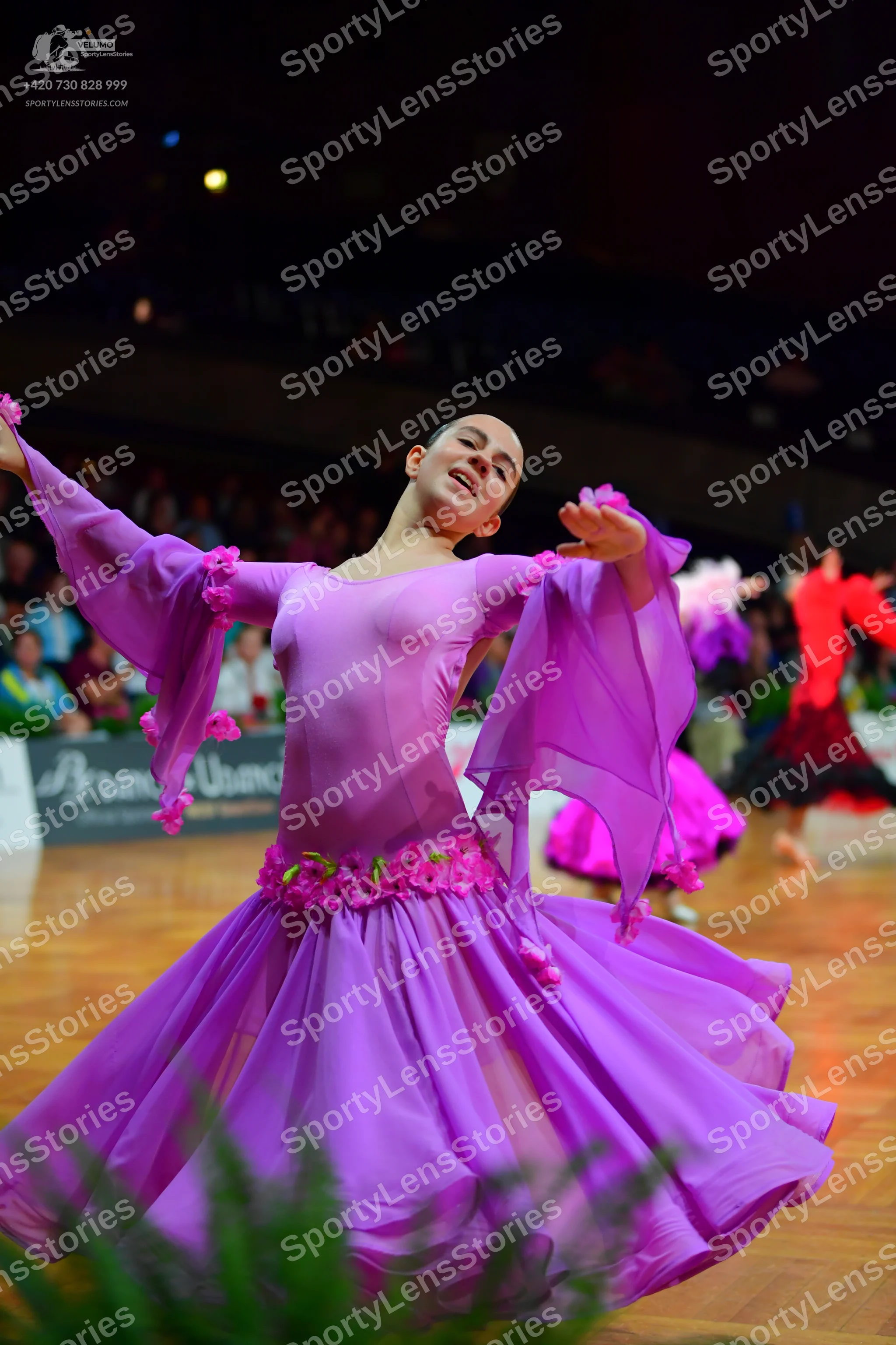 Dancesport competitor: Female dancer in foreground: magenta long-sleeved ballroom dress with large, flo