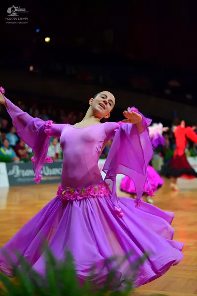 Dancesport competitor: Female dancer in foreground: magenta long-sleeved ballroom dress with large, flo