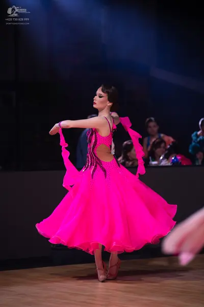 Dancesport competitor: Female dancer: bright pink latin dress with a flowing skirt and black sequin/bea