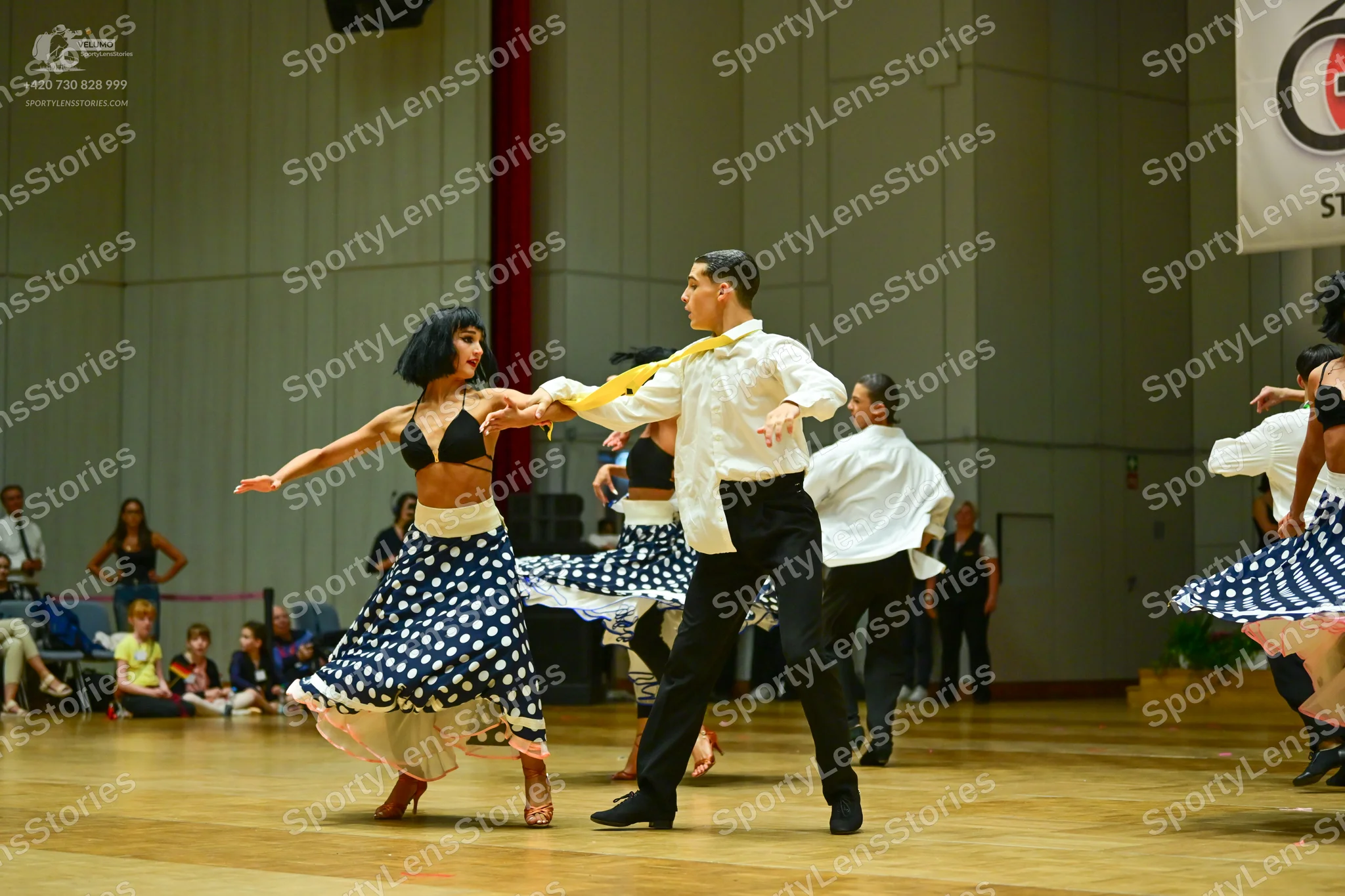Dancesport competitor: Female dancer: black bra-style top, white waistband, and a long skirt with a nav