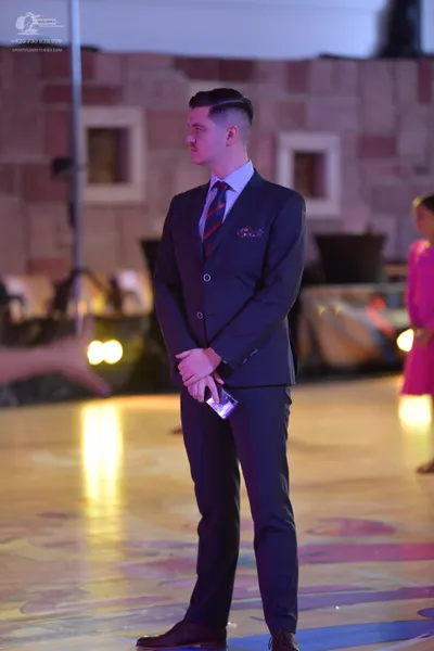 Dancesport competitor: Male dancer: dark navy blue suit, light blue shirt, striped tie, and dark brown 