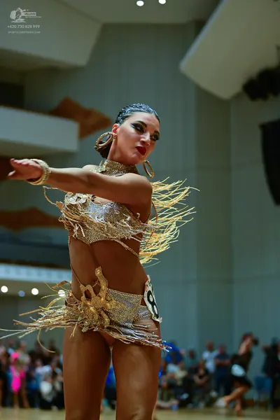 Dancesport competitor: Female dancer: gold, sequined Latin costume with long fringe, large gold hoop ea