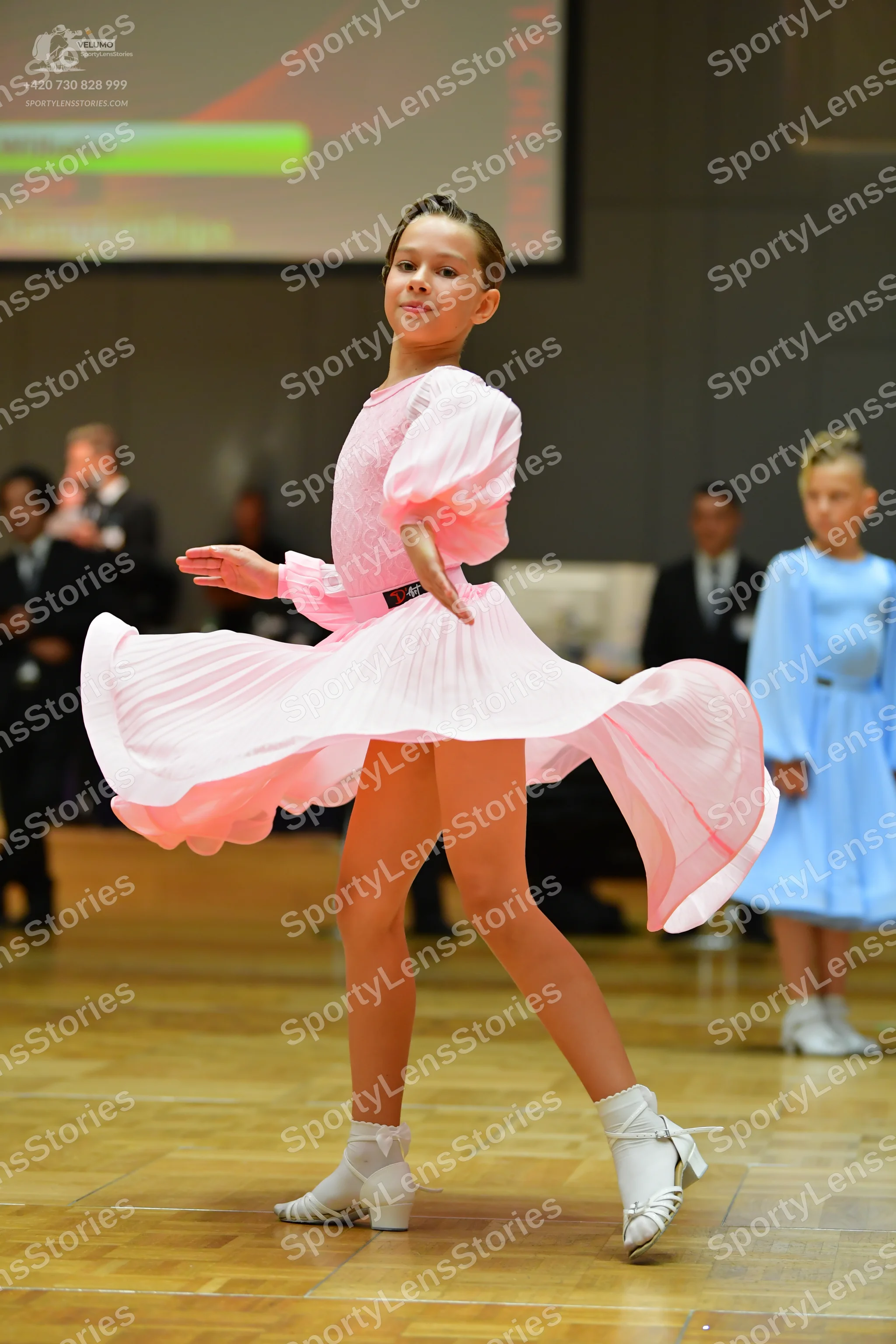 Dancesport competitor: Female dancer in foreground: light pink ballroom dress with long sleeves and a f
