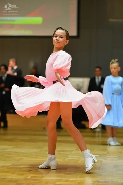 Dancesport competitor: Female dancer in foreground: light pink ballroom dress with long sleeves and a f