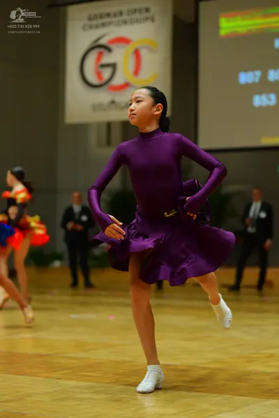 Dancesport competitor: Female dancer in foreground: purple long-sleeved latin dress with a high necklin
